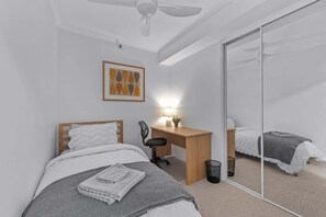 A bedroom with a bed, a desk, a chair, a ceiling fan, a wall-mounted light, and a mirror. - Skyline Stunner! 3bed/2bath/1car/views ~ CBD (Brisbane)