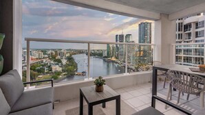 A balcony with a view of a river and cityscape, a small table with a plant, and a seating area with chairs. - Skyline Stunner! 3bed/2bath/1car/views ~ CBD (Brisbane)