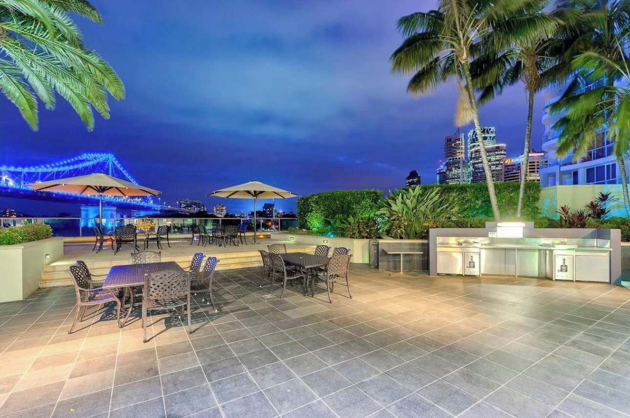 An outdoor patio area with tables and chairs, a bar area, and a view of a city skyline at night.