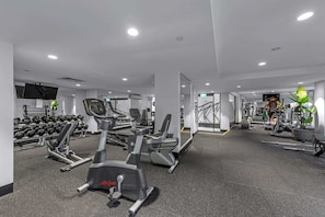 Ein Fitnessstudio mit Cardiogeräten, Kurzhanteln und einem Bildschirm.