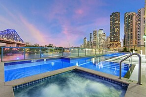 Piscina no terraço com vista para o horizonte urbano, uma ponte e edifícios modernos altos.