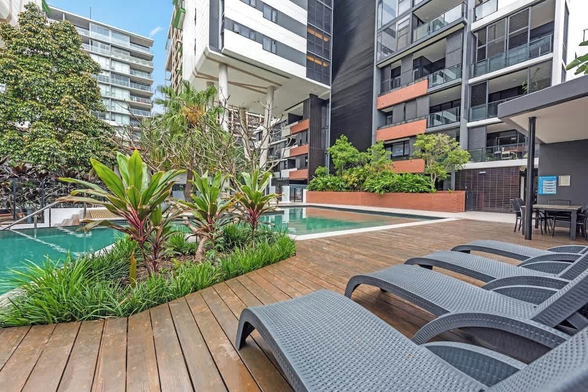 A rooftop pool area with lounge chairs, a wooden deck, and surrounding greenery.