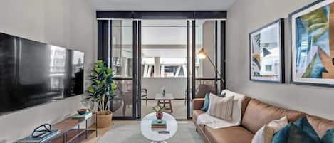 Een moderne woonkamer met een flatscreen televisie, een bank, een salontafel, en een eetgedeelte zichtbaar door glazen deuren.