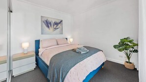 A bedroom with a bed, bedside tables, a wall-mounted artwork, and a potted plant. - City Heights! 2bed/1bath/1car/views ~ CBD (Brisbane)
