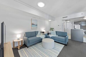A modern living room with a sofa set, a round ottoman, a small side table with a lamp, and a painting on the wall. - City Heights! 2bed/1bath/1car/views ~ CBD (Brisbane)