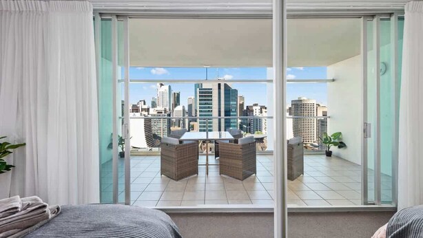 A hotel room with a city view, a balcony with a table and chairs, and a sliding glass door. - City Heights! 2bed/1bath/1car/views ~ CBD (Brisbane)