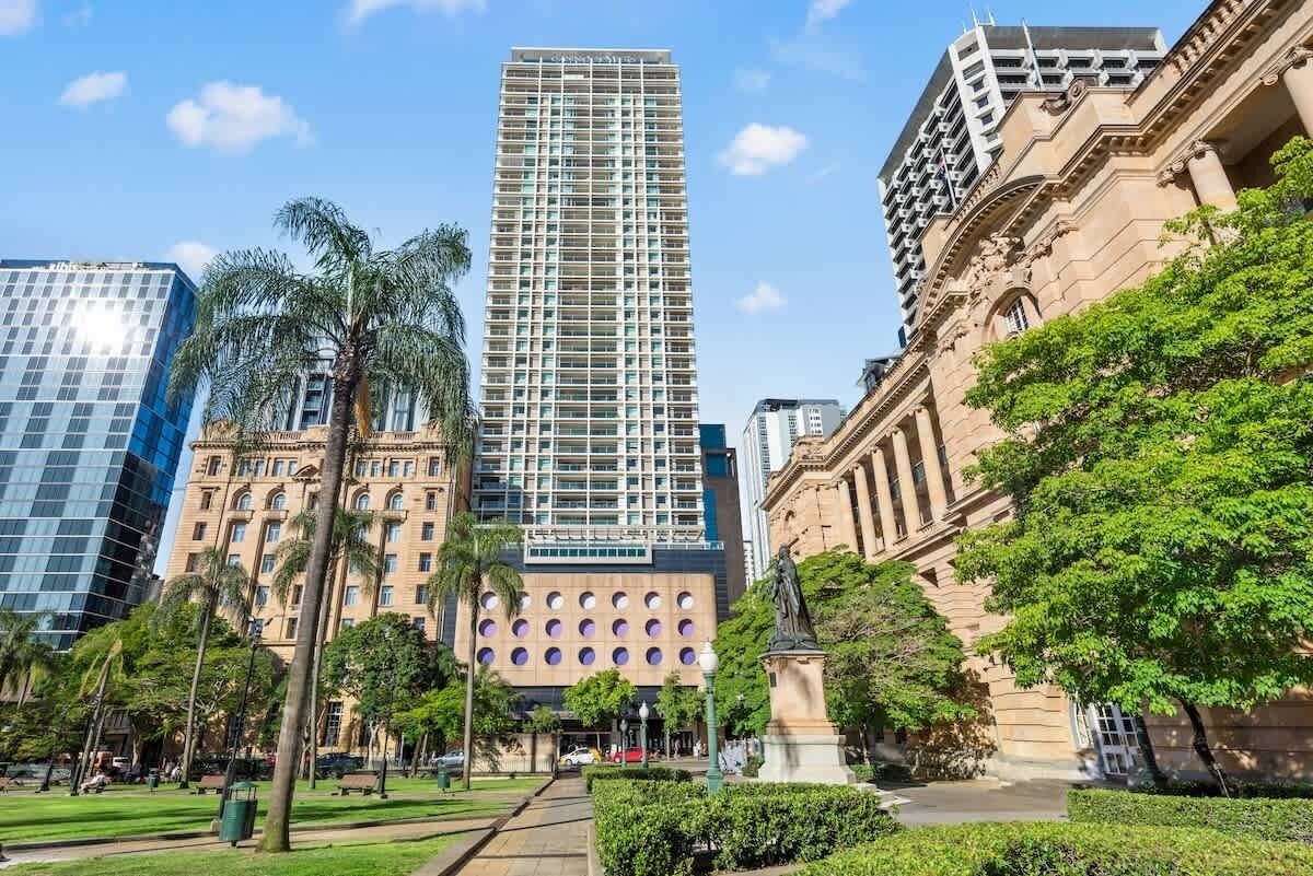 Un edificio alto con una fachada de ventanas enrejada, rodeado de palmeras y una estatua.