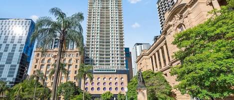Un edificio alto con una fachada de ventanas enrejada, rodeado de palmeras y una estatua.