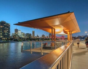 A waterfront promenade with a covered seating area, a view of the city skyline, and a bridge in the background. - Woolstore Elegance ~ 2bed/2bath/1car ~ Teneriffe (Brisbane)