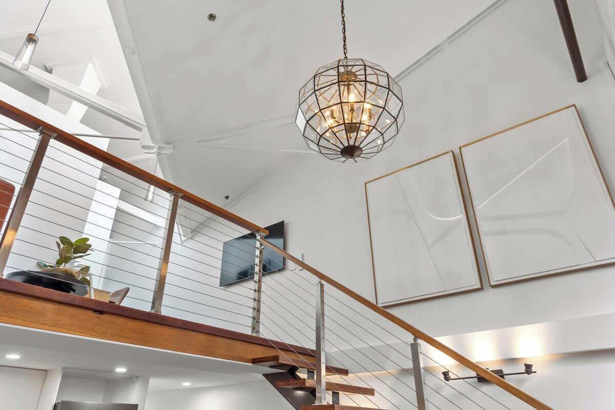 A modern interior with a staircase, a hanging light fixture, and framed artwork on the walls.