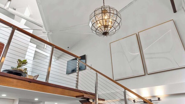 Ein modernes Interieur mit Treppe, einer Pendelleuchte und gerahmten Kunstwerken an den Wänden.