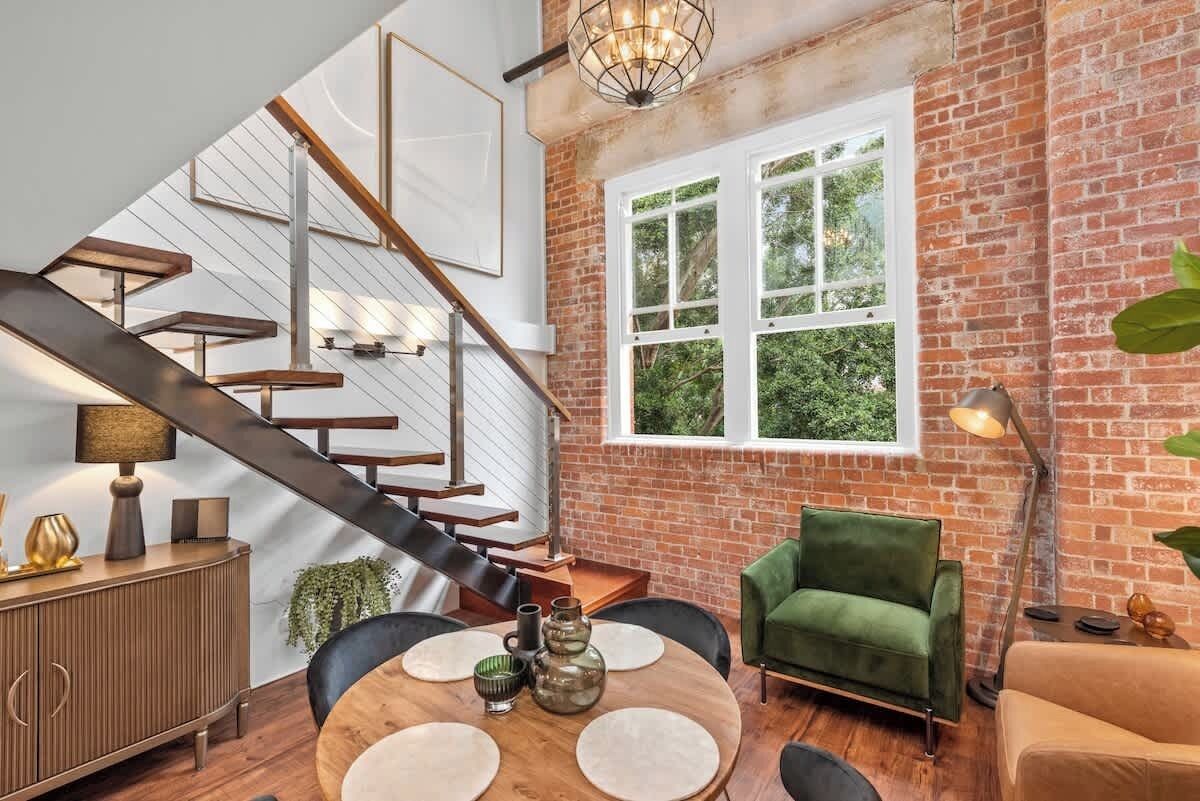 A modern interior with a staircase, a round dining table, and a green sofa.