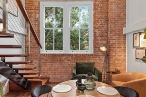 A dining area with a brick wall, a large window, a staircase, and a table with chairs. - Woolstore Elegance ~ 2bed/2bath/1car ~ Teneriffe (Brisbane)