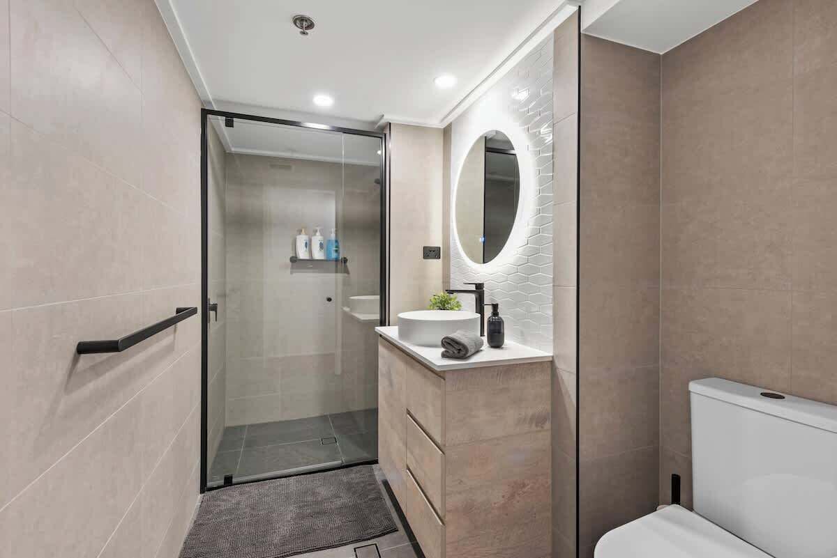 Un bagno moderno con box doccia in vetro, uno specchio rotondo e un water bianco.