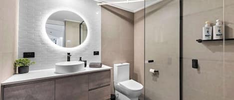 A modern bathroom with a white sink, a toilet, and a glass shower enclosure.