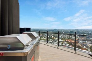 A balcony with a city view, a grill, and a red emergency exit sign. - The Story Suite! 2bed/2bath/2car/pool/views ~ CBD (Brisbane)