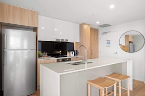 Eine moderne Küche mit einem Edelstahl-Kühlschrank, einer zentralen Kochinsel mit Spüle, Holzausstattung und einem runden Spiegel an der Wand.
