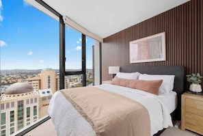 Ein Schlafzimmer mit einem großen Bett, einem Nachttisch, einem gerahmten Bild und Blick auf die Stadt.