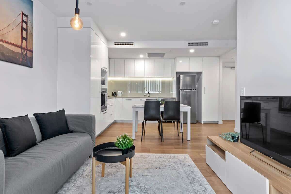 Een moderne woonkamer met een bank, een televisie, een eethoek met stoelen, en een keuken op de achtergrond.