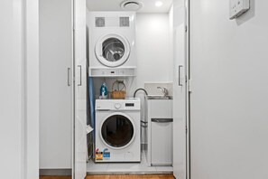 Une petite buanderie équipée d’un lave-linge et d’un sèche-linge à chargement frontal, d’un petit évier et d’un panier posé sur le sèche-linge.