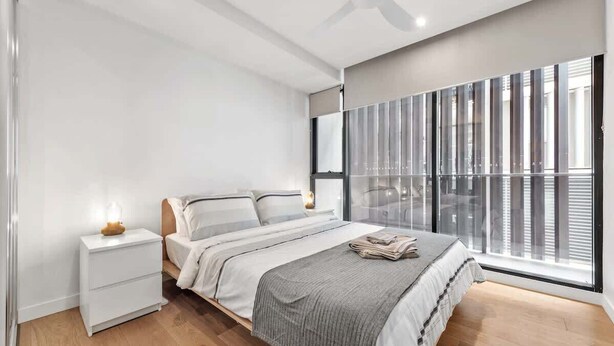 A bedroom with a bed, bedside tables, a ceiling fan, and a large window with blinds. - South Bank Sleek! ~ 1bed/1bath/1car/balcony (Brisbane)