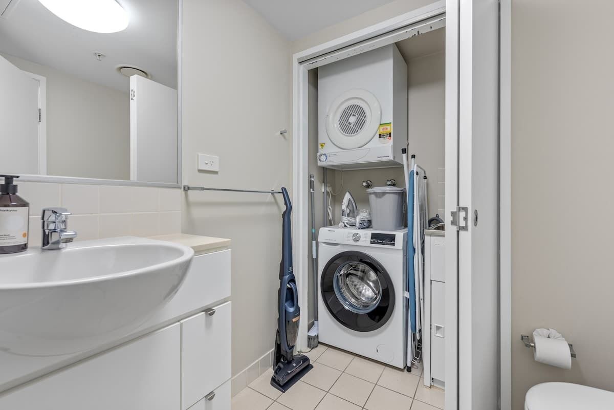 A bathroom with a sink, mirror, washing machine, and toilet.