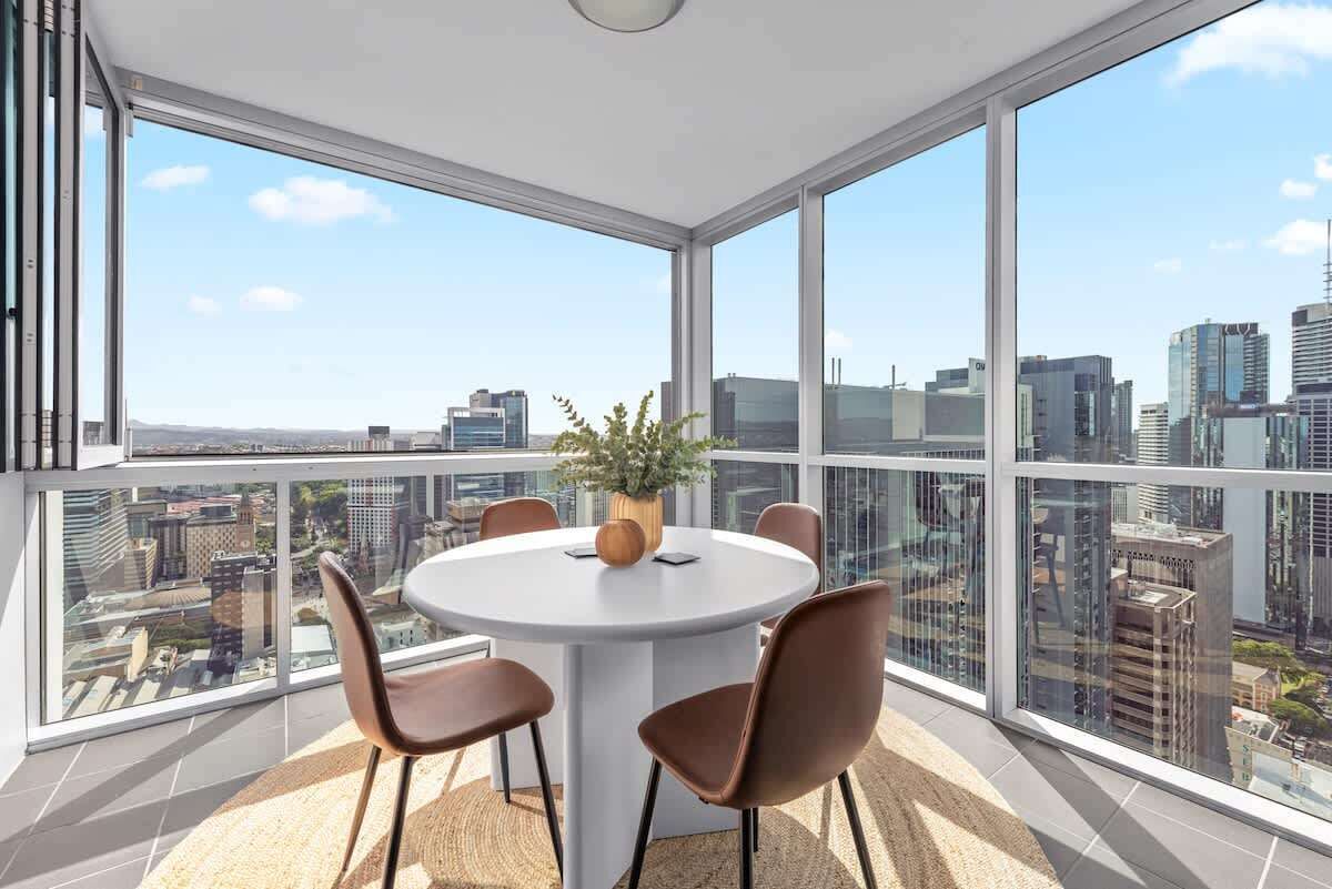 Ein modernes Zimmer mit einem runden Tisch, Stühlen, einer Topfpflanze und großen Fenstern mit Blick auf die Stadt.