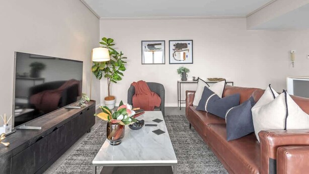 Ein modernes Wohnzimmer mit Flachbildfernseher, einem Couchtisch mit Vase, einer Ledersofa und einer Pflanze.