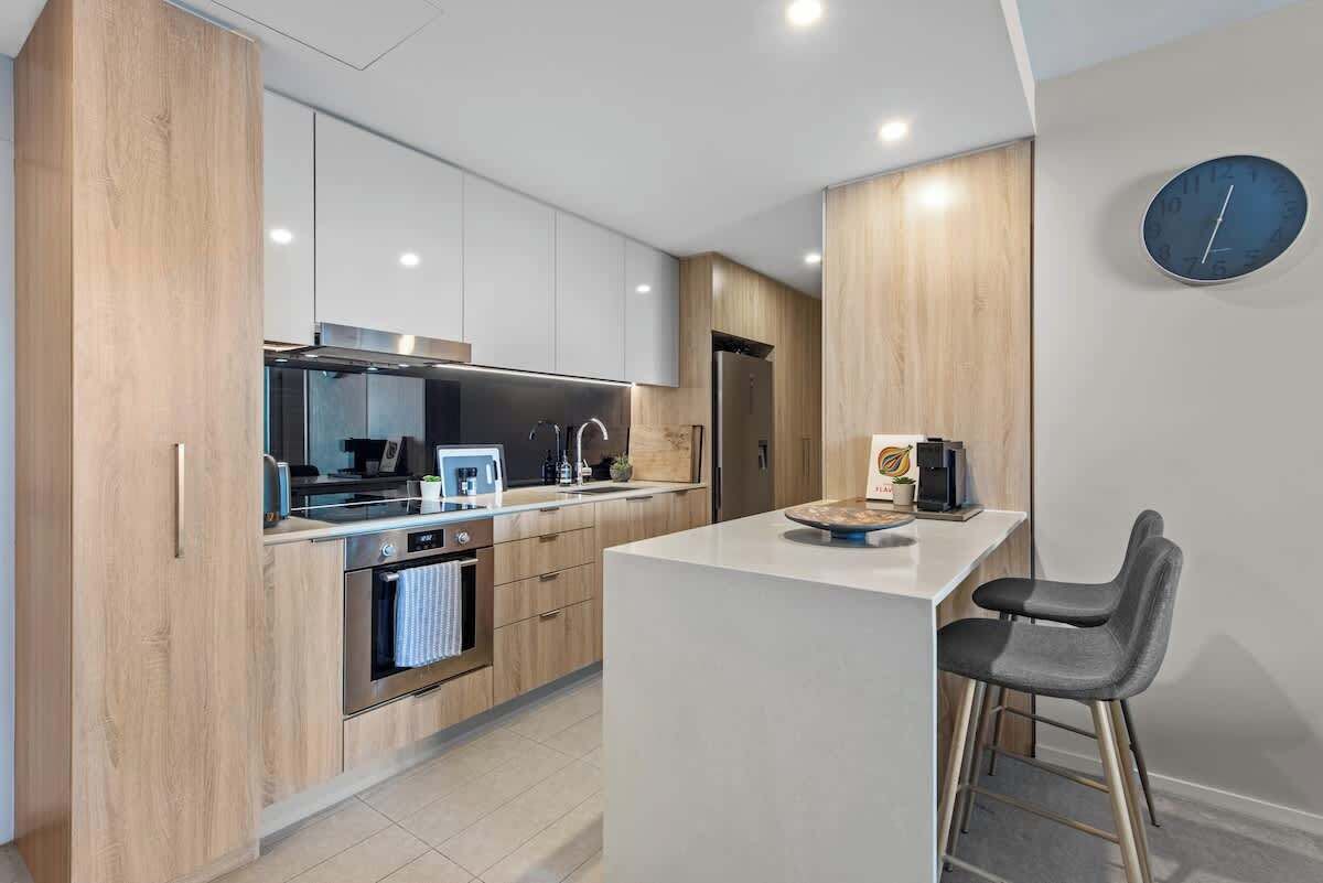 A modern kitchen with wooden cabinets, stainless steel appliances, a central island, and a bar stool.