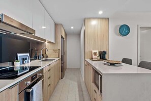 A modern kitchen with wooden cabinets, a built-in oven, a sink, and a clock on the wall. - Top Floor! 2bed/2bath/1car/pool ~ Views ~ CBD (Brisbane)