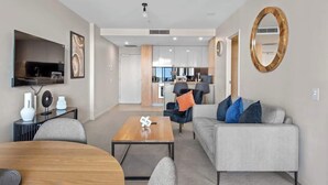 A modern living room with a sofa, coffee table, and TV. There is a kitchen in the background. - Top Floor! 2bed/2bath/1car/pool ~ Views ~ CBD (Brisbane)