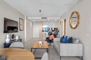 Ein modernes Wohnzimmer mit Sofa, Couchtisch und Fernseher. Im Hintergrund ist eine Küche zu sehen.