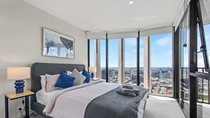 A modern bedroom with a large bed, a nightstand, a city view, and a framed artwork on the wall. - Top Floor! 2bed/2bath/1car/pool ~ Views ~ CBD (Brisbane)