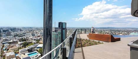 A high-rise building with a clear view of the cityscape, a rooftop terrace with a seating area, and a person standing on the terrace.