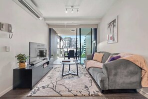A modern living room with a sofa, TV, and a small table. - South Bank Styling! ~ 1bed, 1bath, 1car, Balcony (Brisbane)