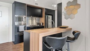 Cozinha moderna com ilha central, armários pretos, eletrodomésticos de aço inoxidável e luminária hexagonal.