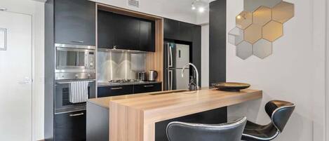 A modern kitchen with a central island, black cabinetry, stainless steel appliances, and a hexagonal light fixture.