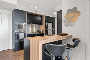 A modern kitchen with a central island, black cabinetry, stainless steel appliances, and a hexagonal light fixture. - South Bank Styling! ~ 1bed, 1bath, 1car, Balcony (Brisbane)