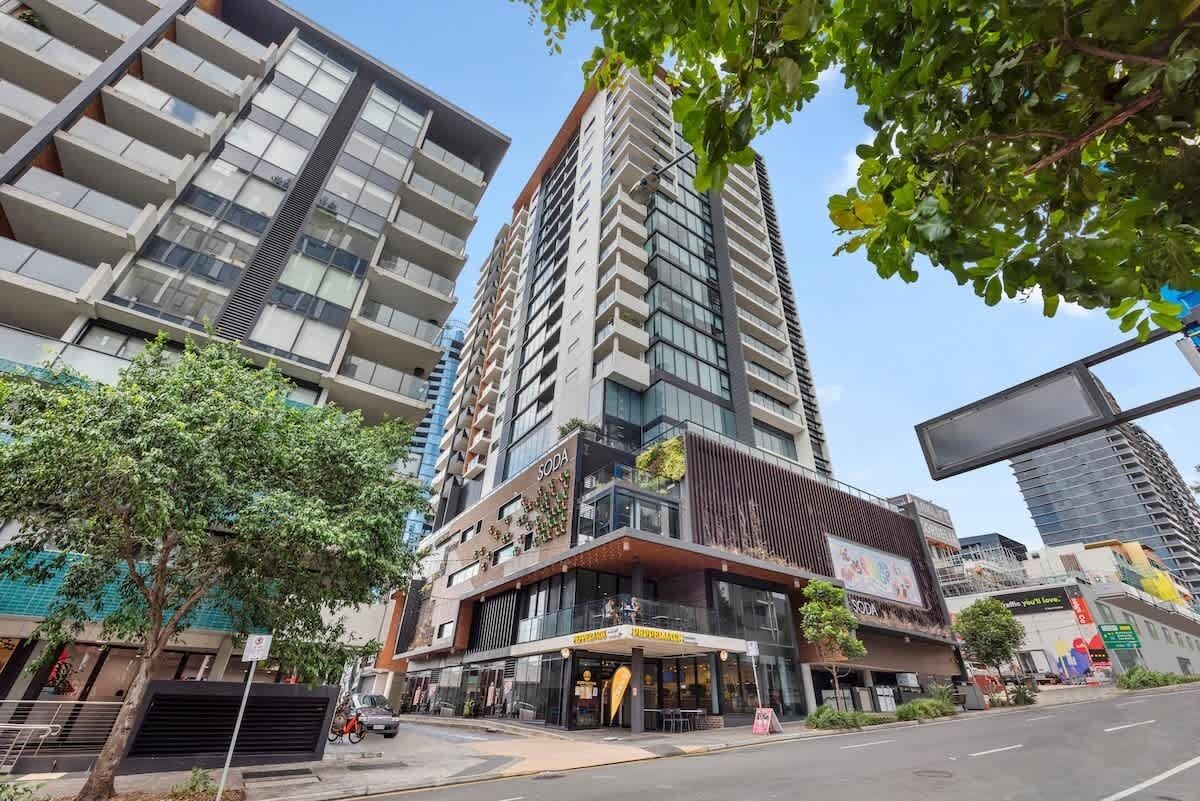 A modern high-rise building with a commercial ground floor, large windows, and a prominent 'SODA' sign.