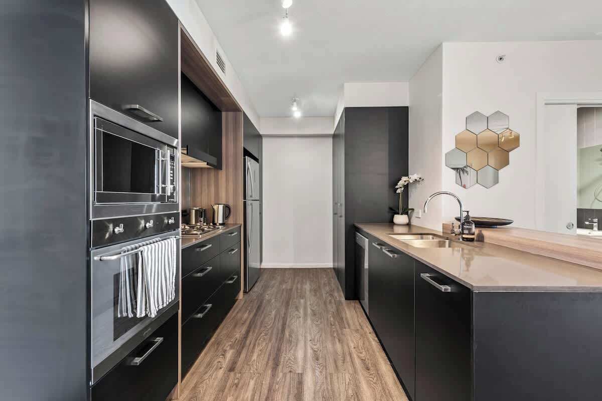 A modern kitchen with dark cabinetry, a wooden floor, and a hexagonal wall decoration.