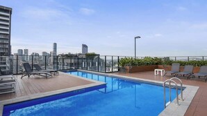 Piscina no terraço com espreguiçadeiras, vista do horizonte da cidade e céu limpo.