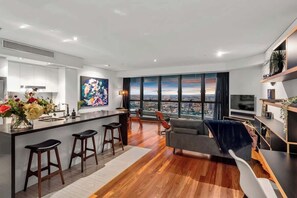 A modern kitchen with a bar area, a dining space with a view, and a living area with a sofa and TV. - Skyhigh Executive! ~ 2bed/2bath/1car/views ~ CBD (Brisbane)
