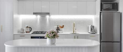 A modern kitchen with white cabinetry, a stainless steel refrigerator, and a central island with a black screen.