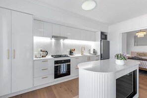 Eine moderne Küche mit weißen Schränken, einer zentralen Kochinsel und einem eingebauten Backofen.