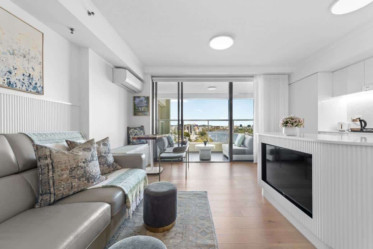 A modern living room with a sofa, ottoman, and a flat-screen TV.