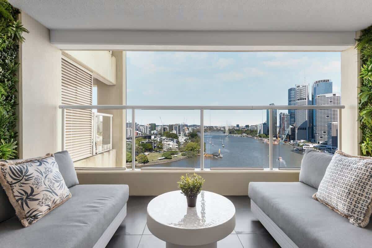 A balcony with a city view, two grey sofas, a round table with a plant, and a railing.