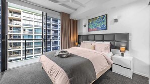 Et moderne hotelværelse med en stor seng, et natbord, en loftsvifte, et maleri og udsigt til en skyskraber.