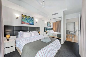 Ein modernes Hotelzimmer mit einem großen Bett, einem Nachttisch mit Lampe, einem Spiegel und einem Gemälde an der Wand.