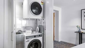 A compact laundry room with a front-loading washer and dryer, a small ironing station, and a basket.