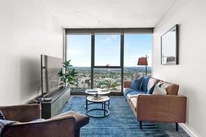 A modern living room with a large window, a sofa, a coffee table, and a TV. - Skyrise Style! 1bed/1bath/1car/views! ~ CBD (Brisbane)